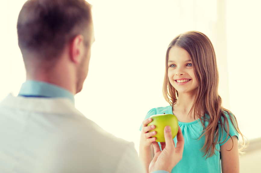 fotografia-menina-sorridente-recebendo-maçâ-verde-de-um-dentista